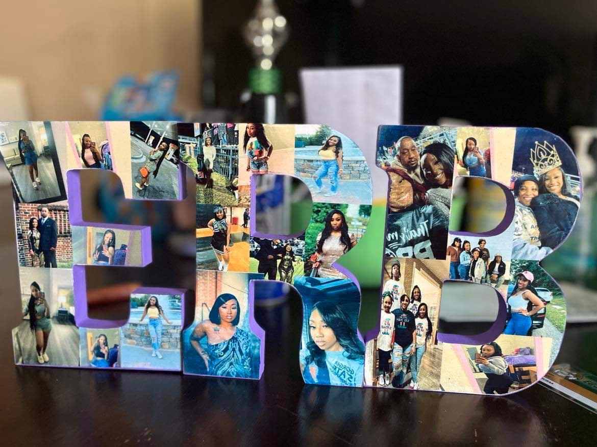 A decorative display featuring custom letters "ERB" from Keep It Sweet & Sassy Designs stands on a surface. Each letter is adorned with a collage of various photos, mostly of people posing, smiling, and enjoying different moments. The personalized touch really shines through against the background of some blurred household items.