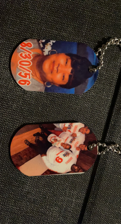 A vertical image showcasing Keep It Sweet & Sassy Designs' Personalized Double-Sided Dog Tags on a dark fabric background. The top personalized accessory features a portrait of a young person with a short haircut, while the bottom tag highlights a group of people in matching white outfits with red lettering, crafted using high-quality sublimation printing.