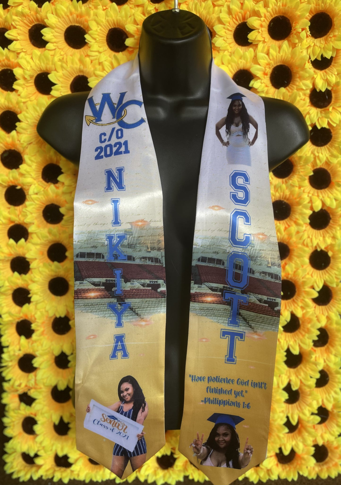 A Custom Grad Stole from Keep It Sweet & Sassy Designs features "WC C/O 2021" and "Nikiya Scott" in blue text, with images of a young woman posing, a stadium, and the Bible verse Philippians 1:6. This special keepsake is displayed on a black mannequin against a sunflower backdrop, celebrating student accomplishment.