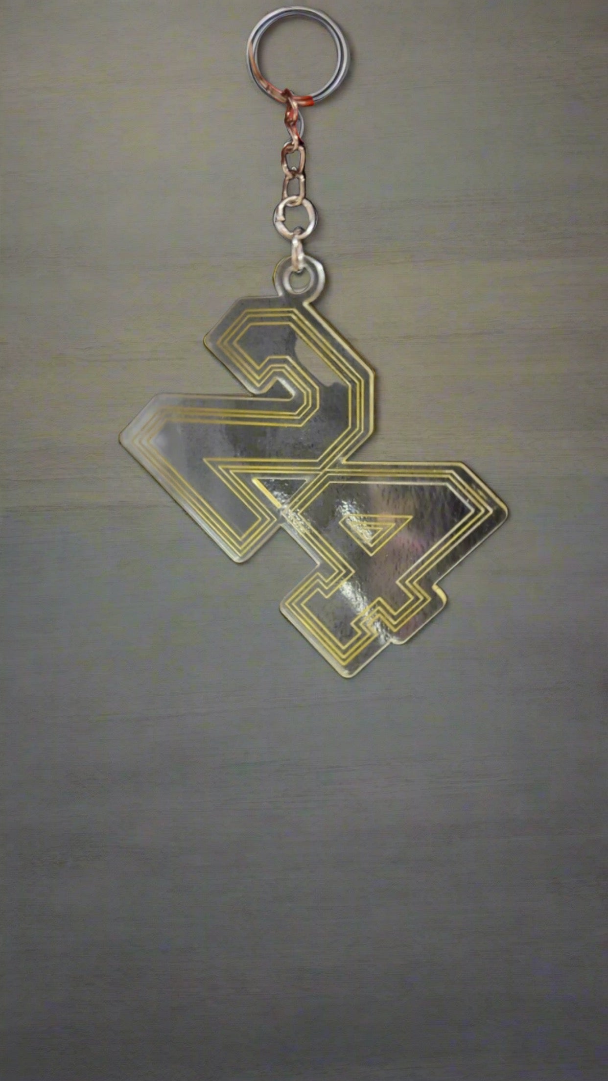 The 24 Grad Keychain from Keep It Sweet & Sassy Designs is a durable acrylic accessory featuring a clear and gold-bordered design of the number "24" against a grey background. Perfect for celebrating a milestone, the numbers are stylized with a geometric pattern and attached to a robust metal chain and ring.